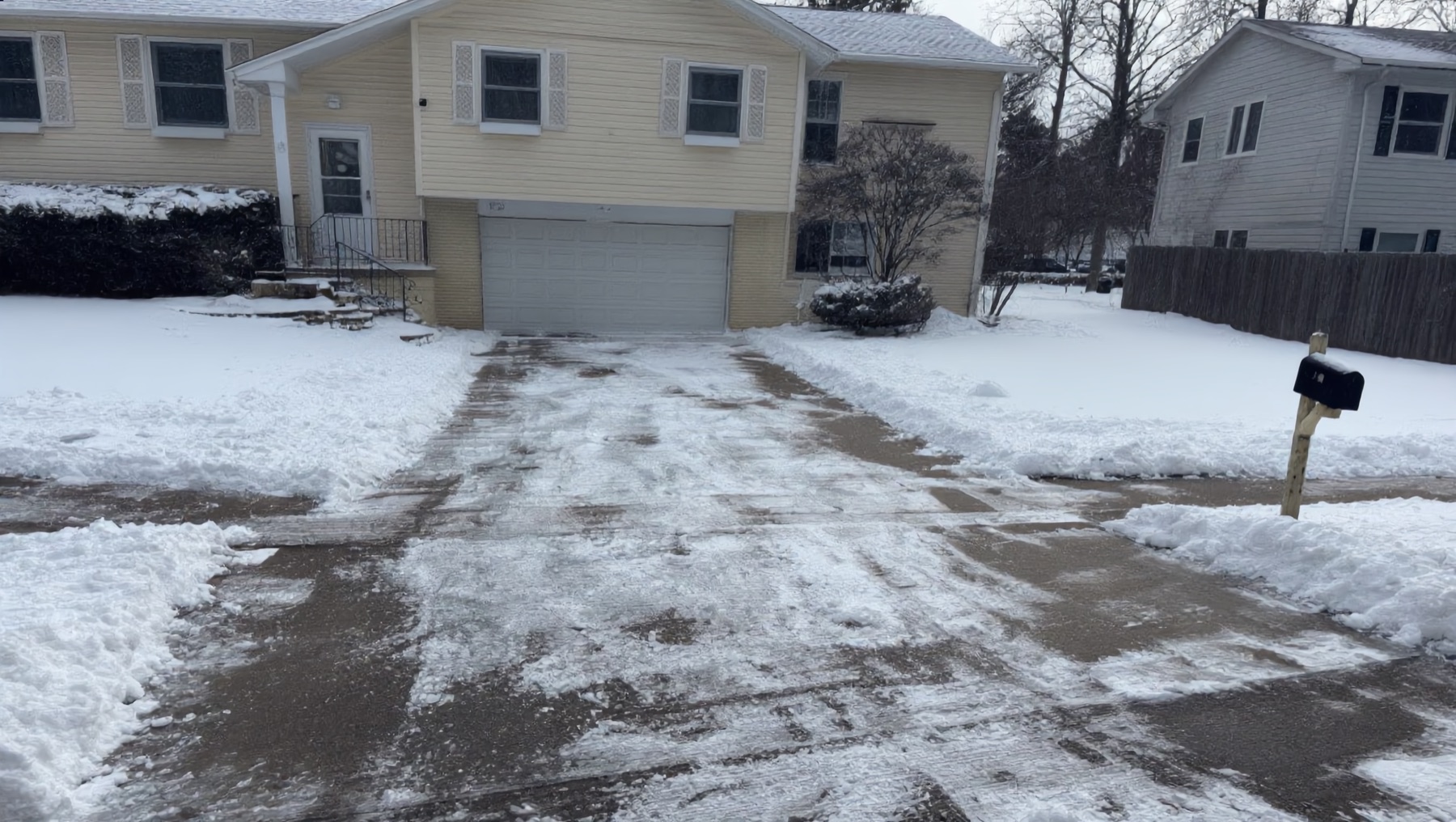 Cleared residential driveway in Eastern Iowa after a winter snowfall, sidewalk shoveled and ice-free on a gray morning